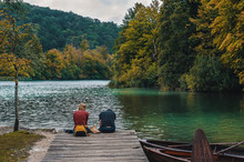 Two People Sitting On A Wooden Pier Over The Lake In The Fall And Meditate While Looking At The Water