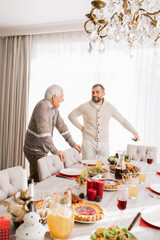 Portrait of smiling mature man talking to his father standing at large dinner table during family celebration