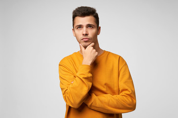 Wall Mural - Handsome attractive young man ponders over a gift for a girl for a new year or birthday, remembers the latest events, thinking of something important holding his chin, looks into the distance