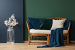 © Photographee.eu - Blue blanket and pillows on rattan sofa next to white flowers in green apartment interior. Real photo
