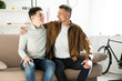 © LIGHTFIELD STUDIOS - happy father and teen son hugging on sofa at home, looking at each other