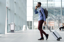 Side Portrait Of Young African Man Traveling With Suitcase And Cellphone At Airport