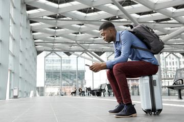 Wall Mural - african american man sitting on suitcase at station with mobile phone