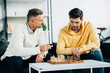 © LIGHTFIELD STUDIOS - son and mature father playing chess together on weekend in living room