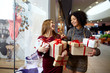 Two mixed race women with gift boxes in hands near storewindow. Multi ethnic girls smiling with presents on christmas new year sale. Caucasian and african american females buy presents for holidays.