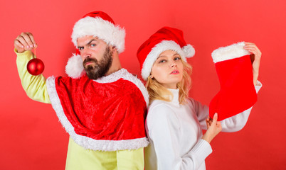 Wall Mural - Couple christmas santa costume hold sock and ornament ball. Woman and bearded man in santa hat waiting christmas red background. Christmas celebration concept. Christmas stocking tradition