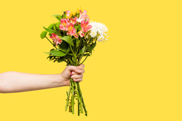 cropped shot of person holding beautiful bouquet of flowers isolated on yellow
