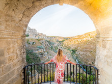 Young Blonde Girl Looking Out Over The  Landscape Of The Sassi Di Matera, Prehistoric Historic Center, UNESCO World Heritage Site, European Capital Of Culture 2019 (wide)