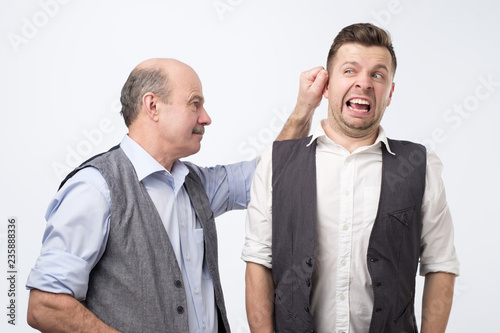 Fényképezés Senior boss pulling young man ear, punishing for mistake at work.