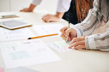 Wall Mural - crop shot of woman taking notes on sticker while working with man in team at table creating modern d