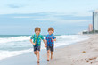 © Irina Schmidt - Two happy little kids boys running on the beach of ocean. Funny cute children, sibling and best friends making vacations and enjoying summer on stormy windy day. Healthy kids on beach of Miami, USA