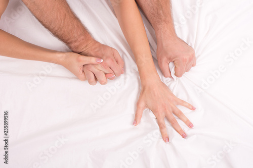 Photographie couple making love in bed on white crumpled sheet, focus on hands