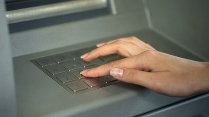 Wall Mural - Woman entering PIN number to check bank account and withdraw money from ATM