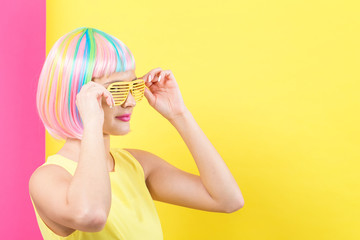 Wall Mural - Young woman in a colorful wig with shutter shades sunglasses on a split yellow and pink background