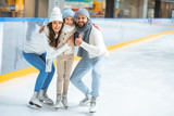 smiling parents and daughter in sweaters looking at camera on skating rink
