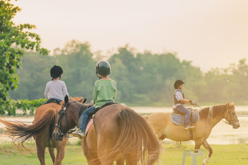 Kids learn to ride a horse near the river before sunset.