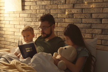 Wall Mural - Father reading Bible to his little children in bed