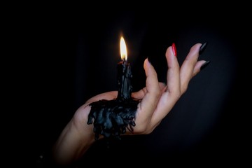 Black Candle melted on hand in black background. For halloween's concept. Felling darkness with light of flame burning from the supernatural.