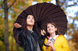 © soleg - Two girls are together under umbrella in autumn city park. Bright yellow leaves.
