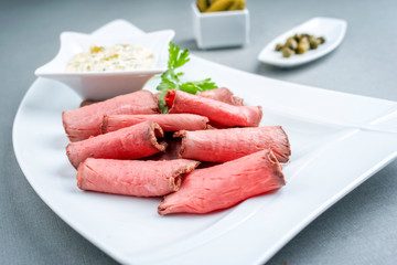 Traditional lunch meat with sliced cold cuts roast beef and remoulade as closeup on a white plate