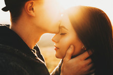Side View Of Crop Male Kissing Pretty Girlfriend In Forehead While Spending Time In Nature On Sunny Day.Crop Guy Kissing Girlfriend In Forehead In Nature