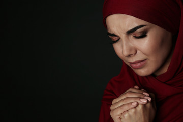 Portrait of sad Muslim woman in hijab  praying on dark background. Space for text