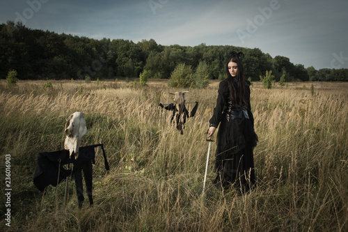 Fotografía Gothic girl with a sword in her hands next to the skull of a cow on a pole