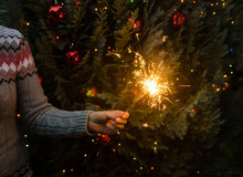 Woman In Knitted Sweater Holding Sparklers Before Christmas Tree