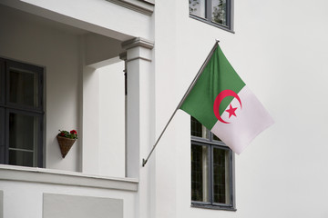 Wall Mural - Algeria flag hanging on a pole in front of the house. National flag waving on a home displaying on a pole on a front door of a building and raised at a full staff.