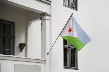 Wall Mural - Djibouti flag hanging on a pole in front of the house. National flag waving on a home displaying on a pole on a front door of a building and raised at a full staff.