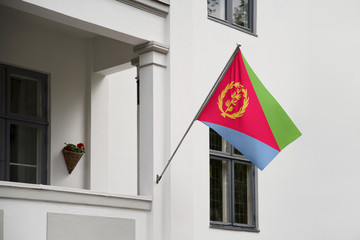 Wall Mural - Eritrea flag hanging on a pole in front of the house. National flag waving on a home displaying on a pole on a front door of a building and raised at a full staff.