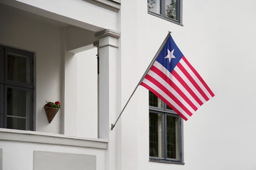 Wall Mural - Liberia flag hanging on a pole in front of the house. National flag waving on a home displaying on a pole on a front door of a building and raised at a full staff.