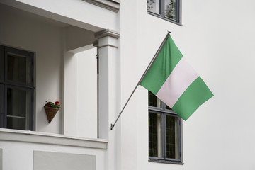 Wall Mural - Nigeria flag hanging on a pole in front of the house. National flag waving on a home displaying on a pole on a front door of a building and raised at a full staff.