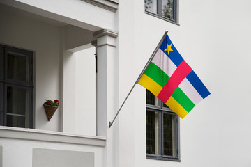 Wall Mural - Central African Republic flag hanging on a pole in front of the house. National flag waving on a home displaying on a pole on a front door of a building and raised at a full staff.