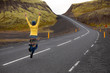 The girl in yellow happily walks and jumps on the asphalt road. Early morning day in Iceland. Car tourism in Iceland.