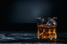 Glass Of Whisky With Ice On Wooden Table Against Dark Background