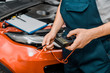 © LIGHTFIELD STUDIOS - cropped shot of auto mechanic holding multimeter voltmeter for car battery voltage checking at mechanic shop