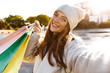 © Drobot Dean - Redhead happy woman walking outdoors holding shopping bags take a selfie by camera.