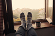 Füße mit Wollsocken liegen auf einer Fensterbank mit Blick in die Berge