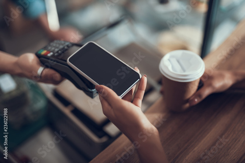Fotografie, Obraz Hand of young lady placing smartphone on credit card payment machine