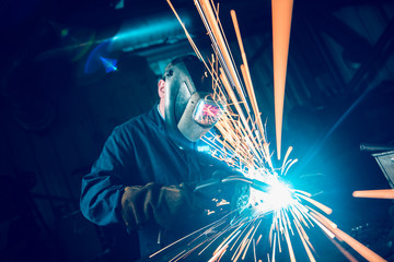 london, england, 02/02/2018 A vibrant action shot of a skilled working metal welder in action, welding metal. Photographed with a slow shutter speed and spark trails. Orange and teal.