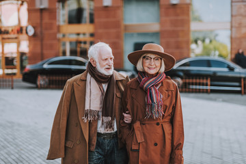 Wall Mural - Portrait of handsome bearded man holding hand of his wife while looking at her and smiling. Lady wearing hat and glasses