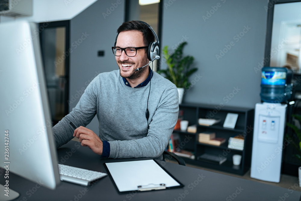 Portrait of a handsome smiling man with headset working on the computer. - obrazy, fototapety, plakaty 