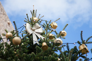 Wall Mural - Christmas tree with silver bows, golden ornaments outside at background of blue sky.