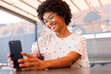 Wall Mural - Happy girl posting new content in social media. Beautiful woman chatting from outdoor cafe.