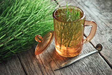 Wall Mural - Vintage glass cup of healthy tea or infusion and bunch of horsetail herbs on wooden table. Herbal medicine.