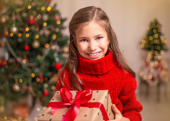 Cute little child girl with present gift box near Christmas tree at home.