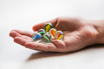 Wall Mural - Colorful game marbles in the hand of a child on white background