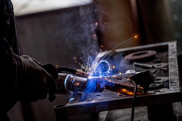 Male worker wearing protective gloves while repairing car exhaust pipe with welding machine