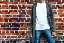 Fashionable Man Wearing Modern Stylish Casual Outfit With Grey Hoodie, Blue Jeans And White T-shirt Posing Near Brick Wall. Shopping Concept.